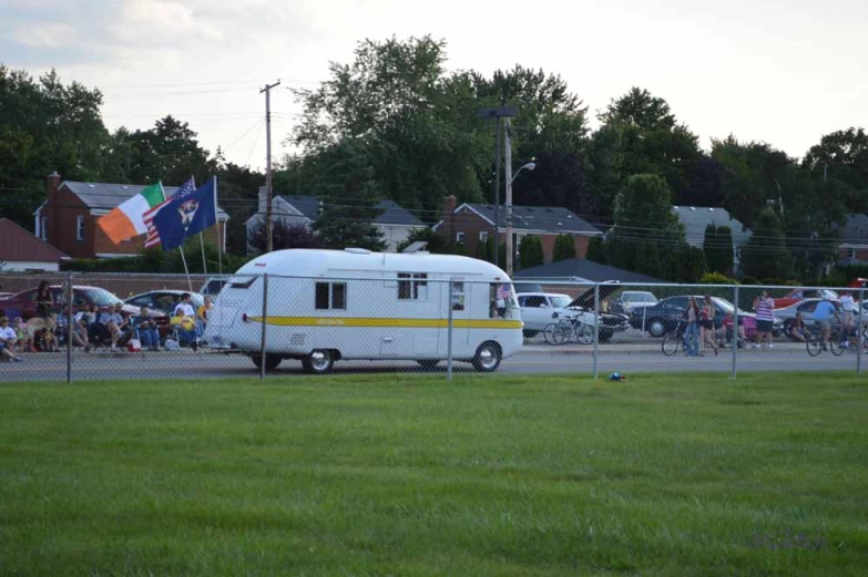 small recreational vehicle parked in a field while people are gathered nearby
