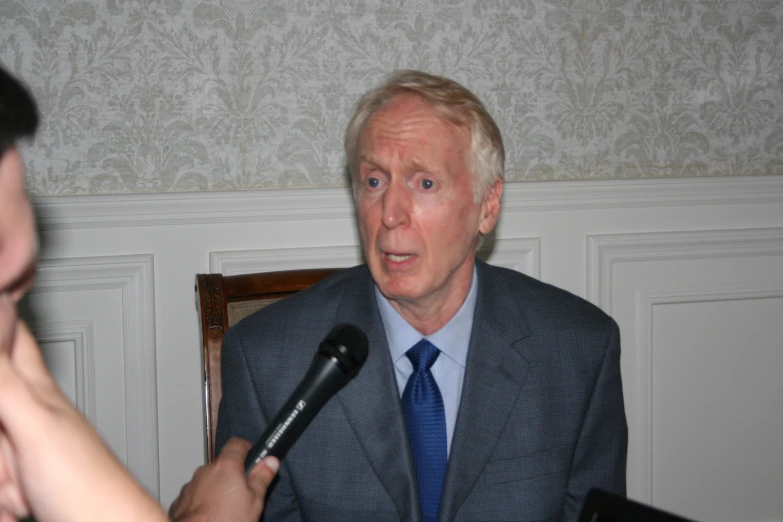 man with microphone on chair at table talking to camera operator