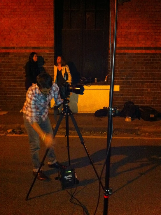 the boy is standing by a tripod, shooting a scene with his camera