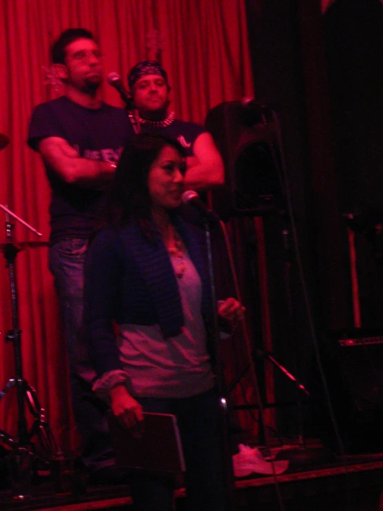 two men and one woman standing on stage with band equipment