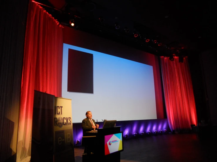 the man stands behind a podium talking on stage