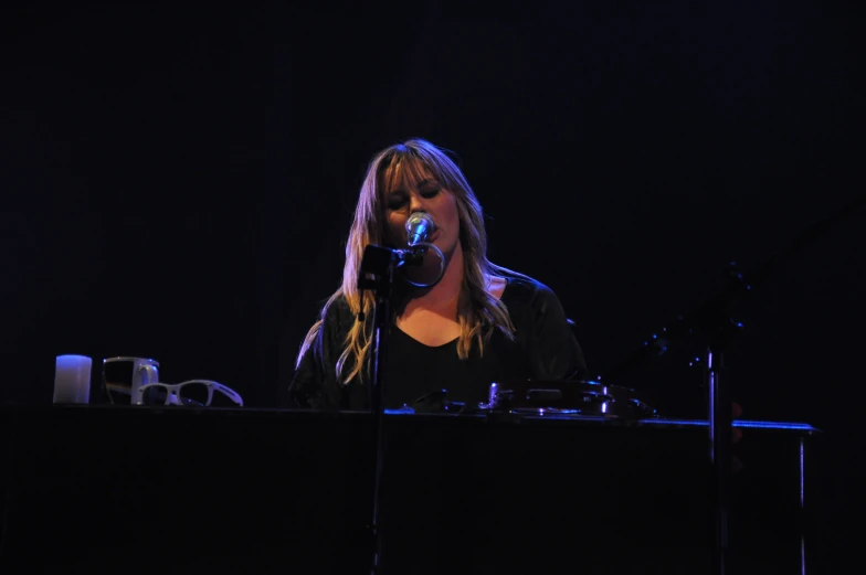 a woman singing into a microphone while sitting in front of a keyboard