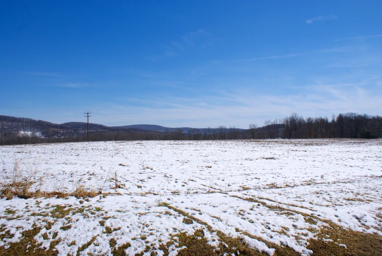 a fenced in snow covered field with telephone poles and hills