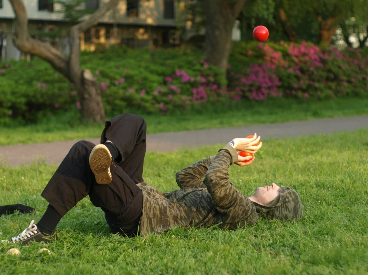 a man in camouflage and sneakers lays down in a grassy area