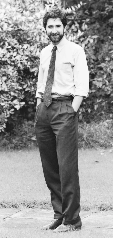 a man smiles while wearing a tie and dress pants