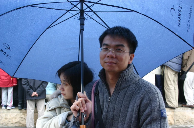 an asian man and woman standing under an umbrella