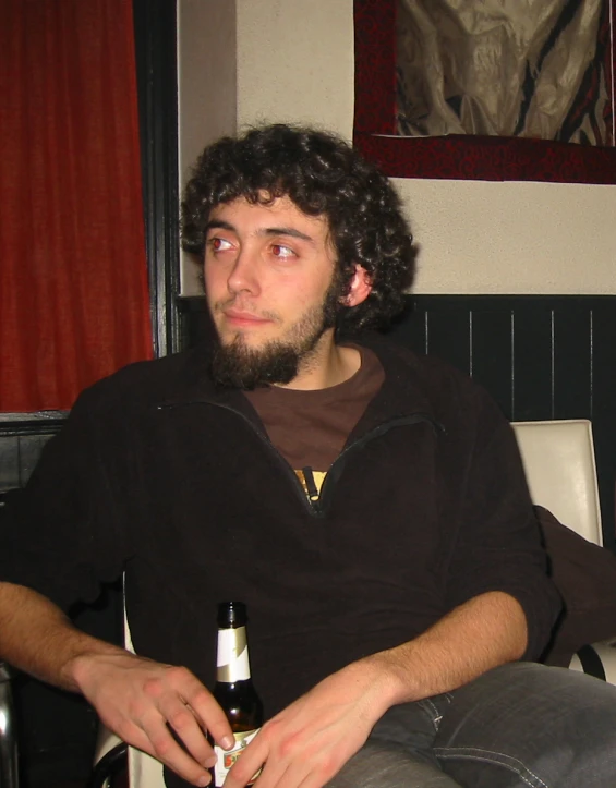 a man with curly hair sitting and holding a beer bottle