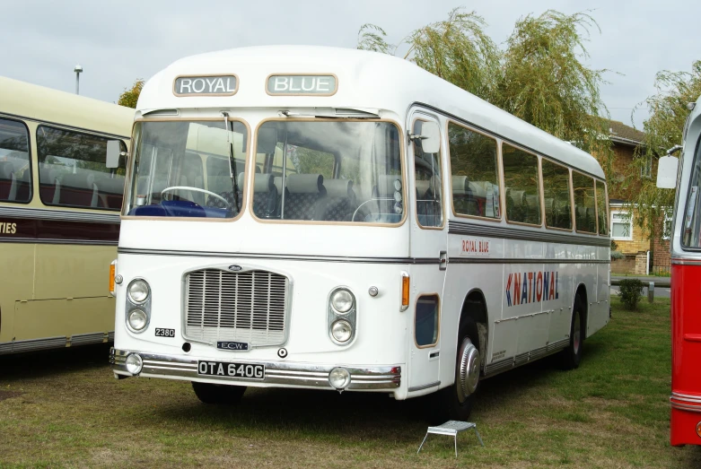 the old white bus is parked next to a red and beige bus