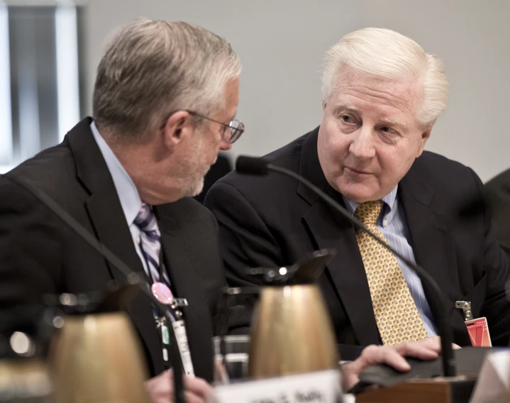 a few men sitting around a table while one man speaks