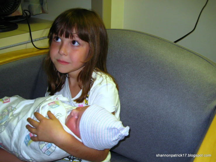 a little girl holding her baby doll in a chair