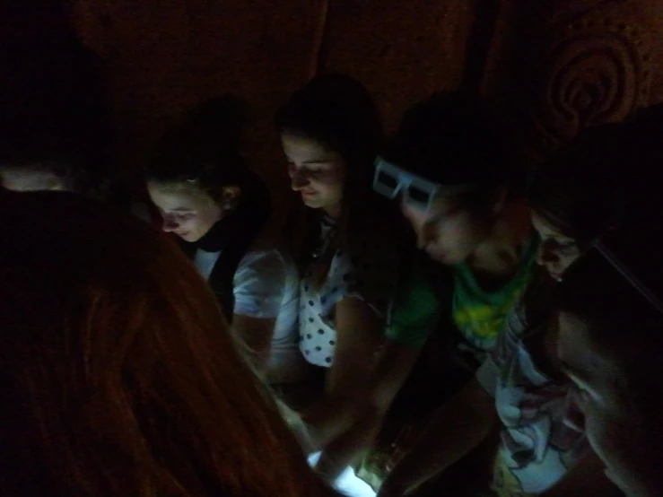 four people looking at a digital device in a dark room