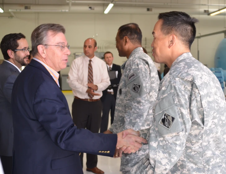 a man in a suit shakes a smiling soldier's hand