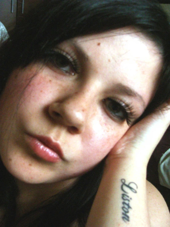 a close - up of a woman's face with a small tattoo on her left wrist