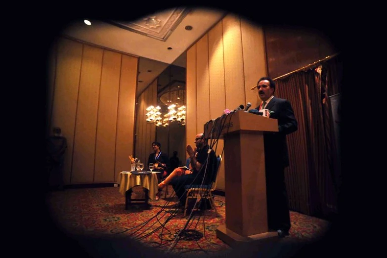 two men at podiums in front of microphones and people sitting down