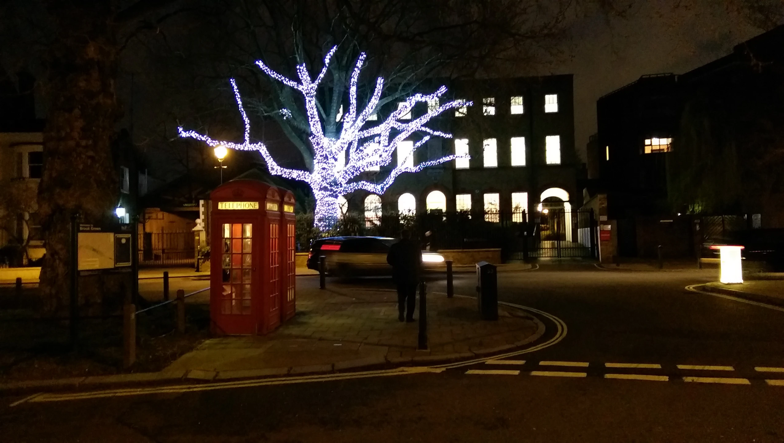 people walk along a path near a street filled with lights and trees