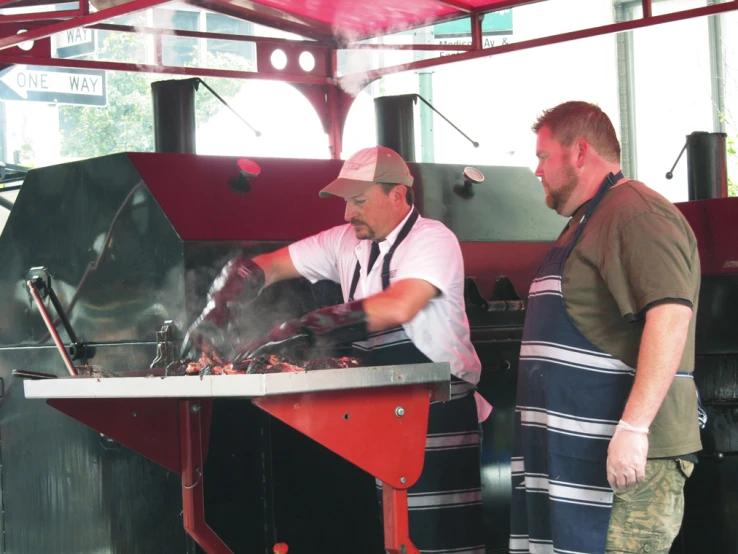 two men cooking meat on an open grill