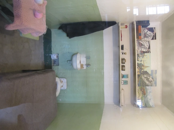 a small, green, white - tiled bathroom with a shelf on the wall and another one on the floor next to it