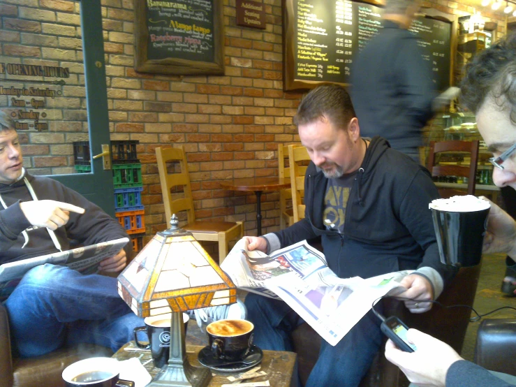 three men reading newspapers and drinking coffee in a restaurant