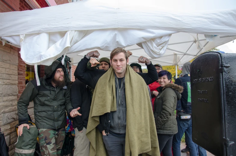 a bunch of men standing under a tent, one holding a towel