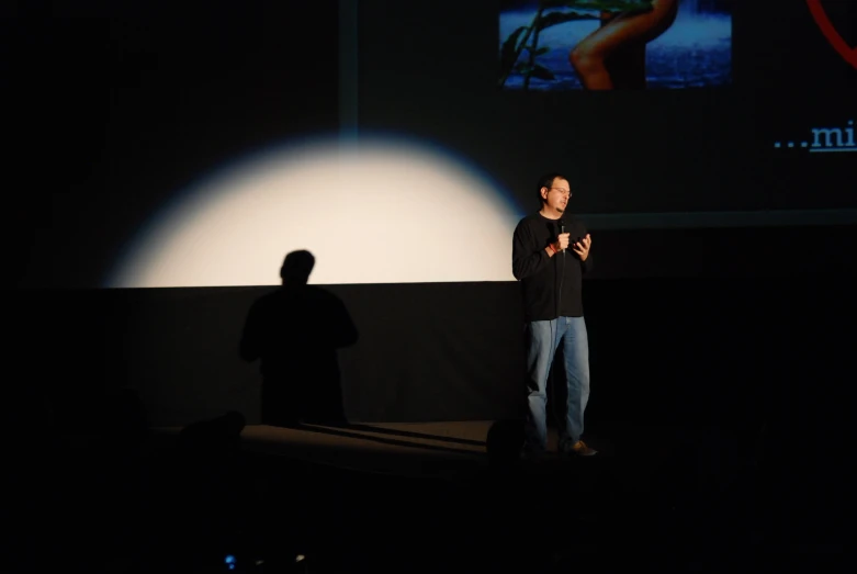 a man standing on stage with projection screen in background