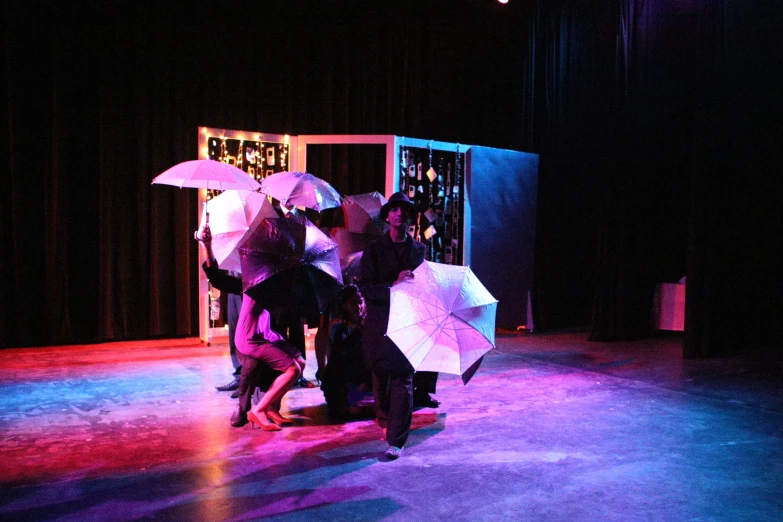 four people are standing under white umbrellas on stage