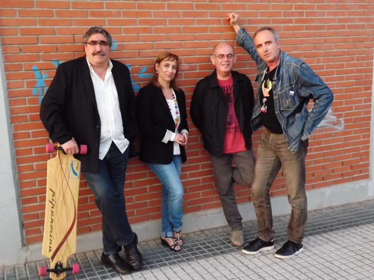 three men and two women leaning against a brick wall