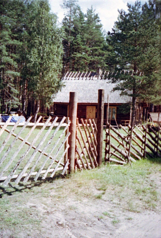 an old cabin sitting next to a wooden fence and trees