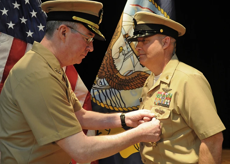 two men in military uniforms stand next to an american flag