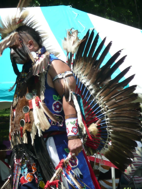 a man wearing an elaborately decorated headdress standing next to a tent