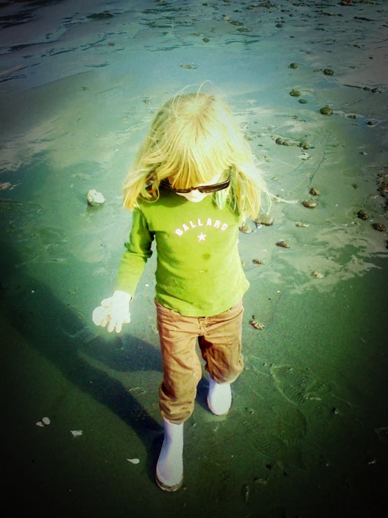 a small girl wearing sunglasses standing in the ocean
