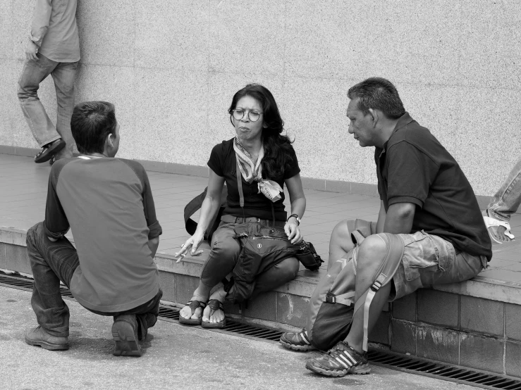 three men are sitting on a wall while a woman talks to them