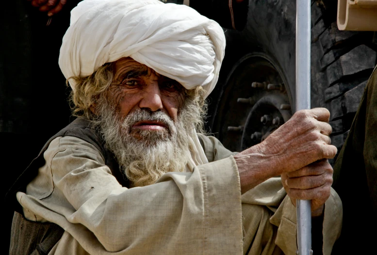 an old man in a turban holds a pole