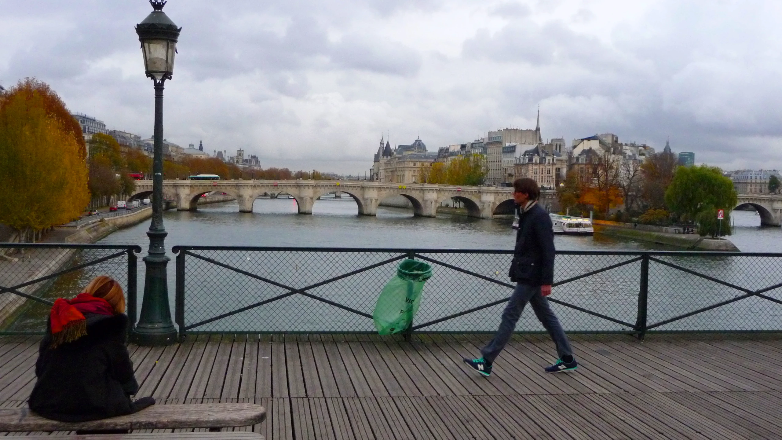 man walking along the river by a bridge in the distance