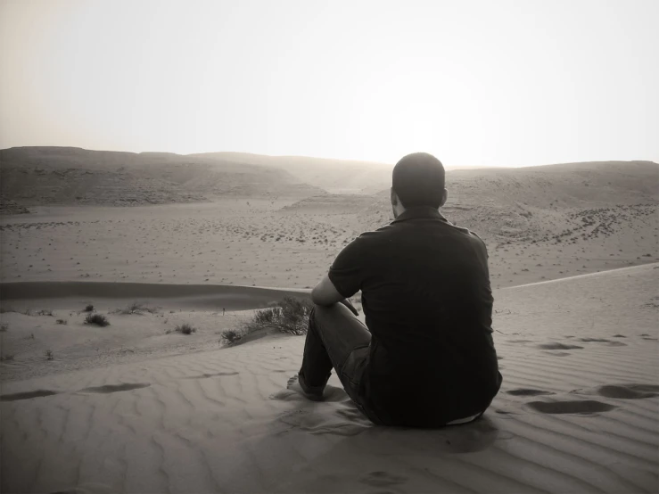 the man sitting in the desert is watching soing