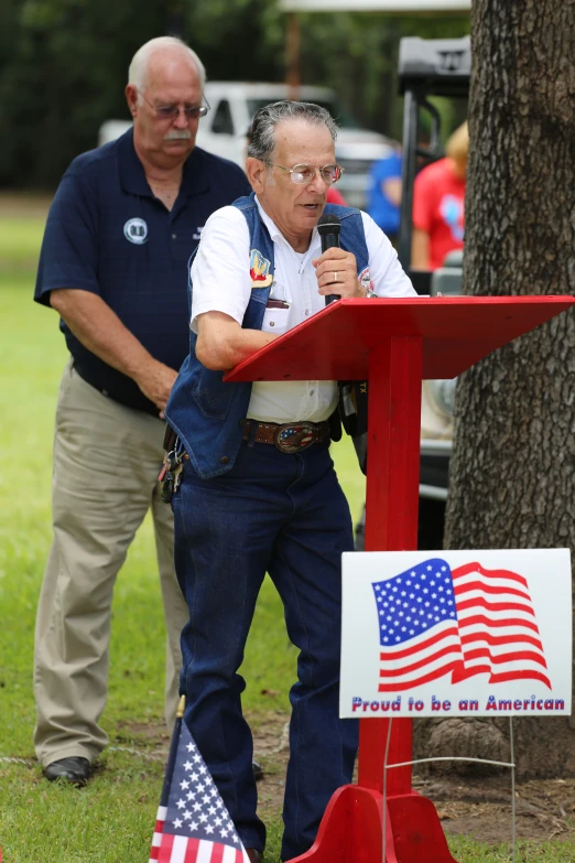 a man giving a speech to two men in front of an american flag