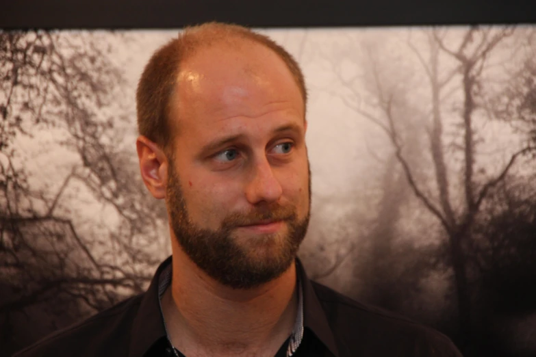 a bearded man with a black shirt and a tree