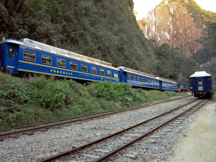 a blue train sitting on the tracks in front of mountains