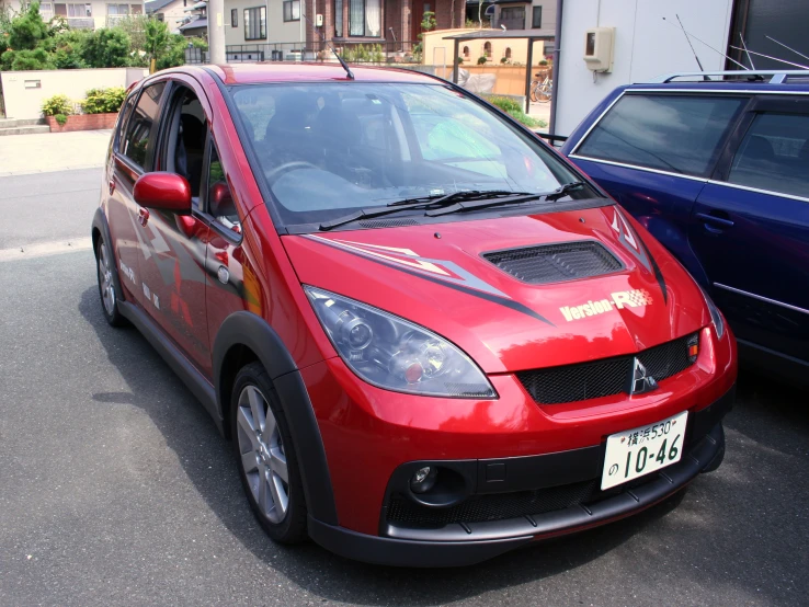 a red car with a warning sticker on it parked in a lot next to another car