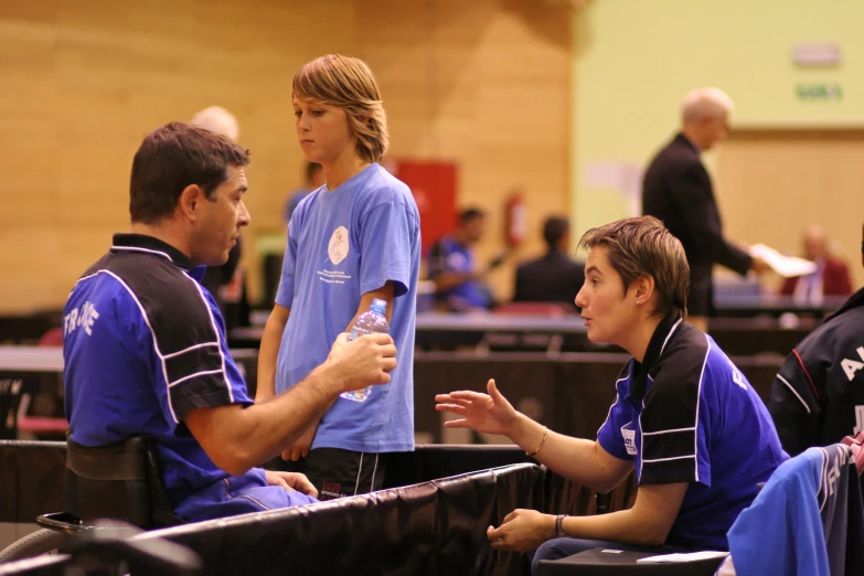 young men and women sitting around a room in blue jerseys