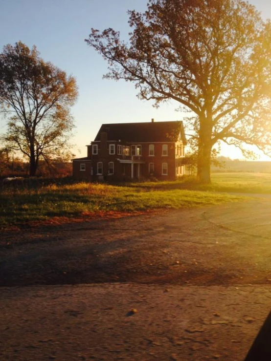 an old house sitting beside trees at sunset