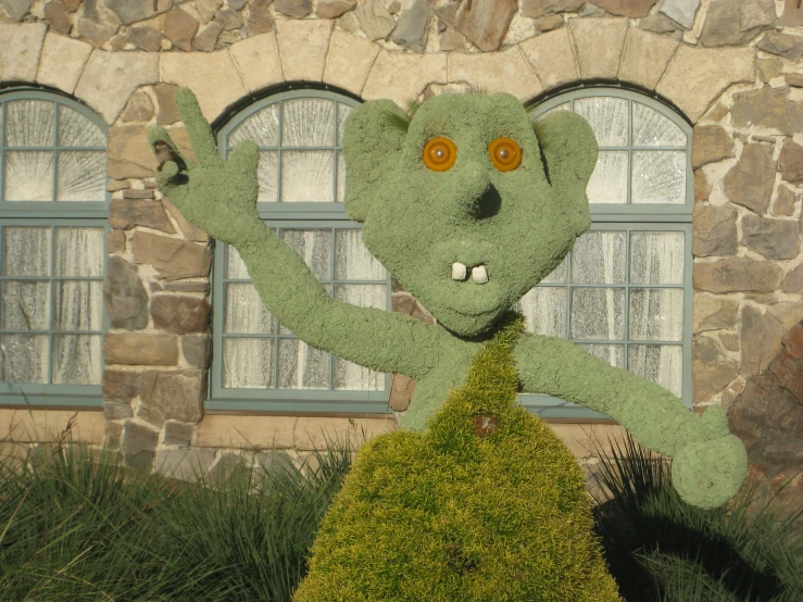 a strange looking teddy bear made of grass in front of a stone building