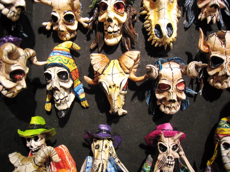 several colorful skulls wearing hats are hanging on a black wall
