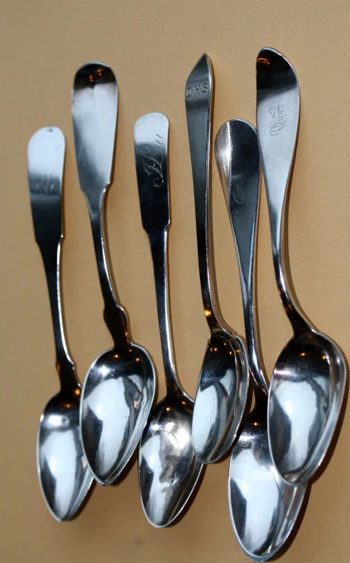 six silver spoons lined up on a tan surface