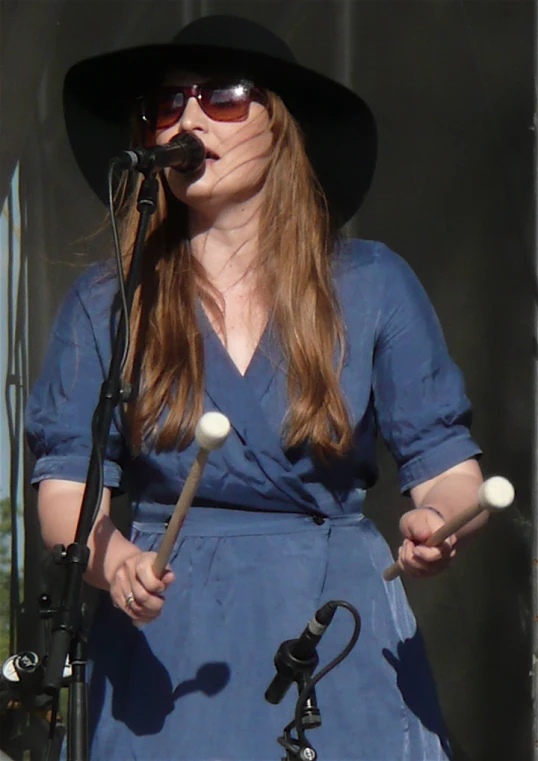 a woman in a hat with drums stands next to a microphone