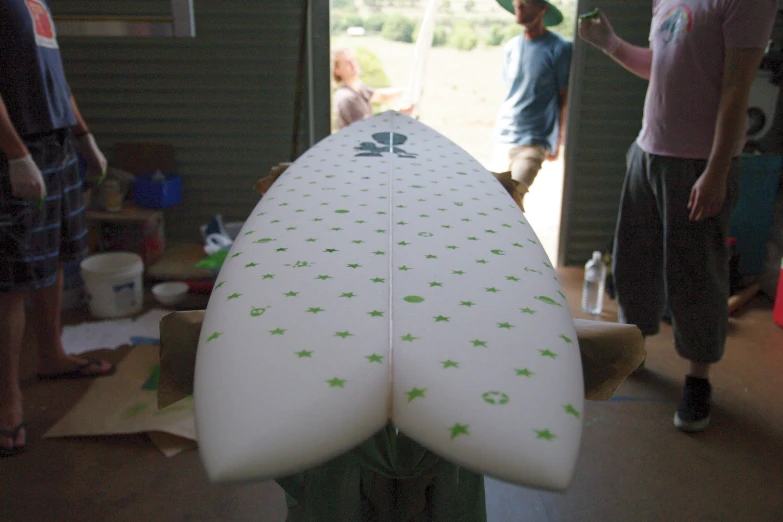 several young people stand around and look at a white surfboard