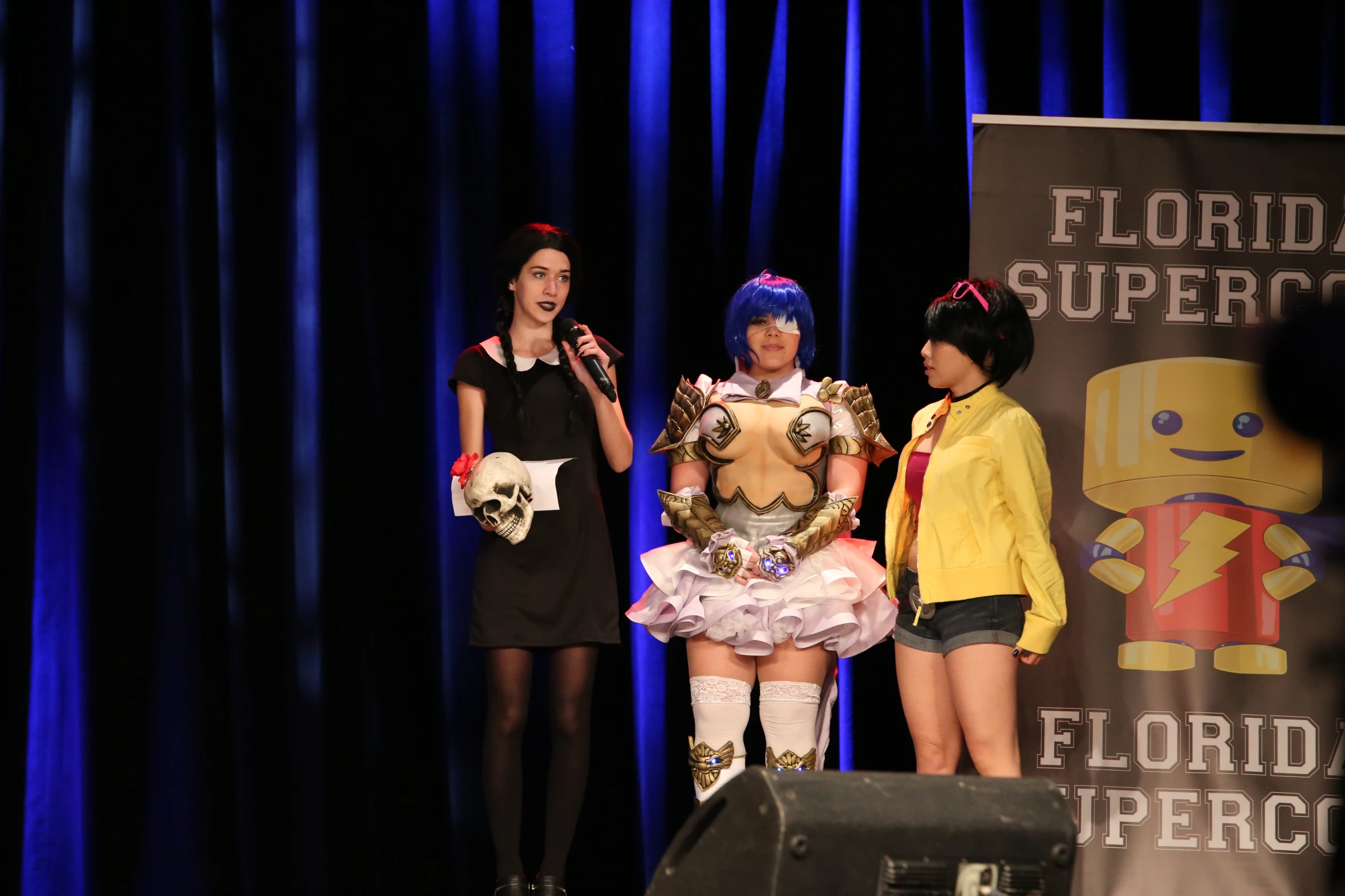 four women in costumes stand on stage with microphones