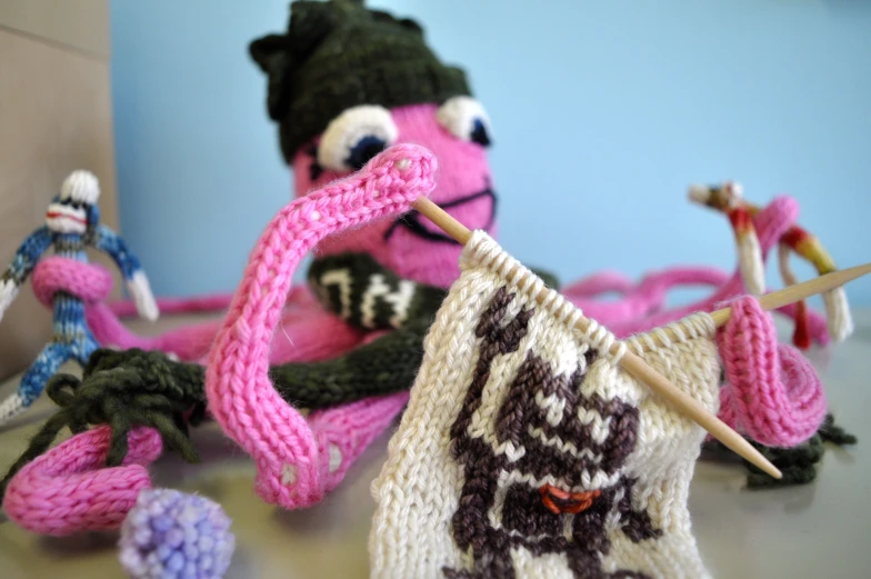 knitted items sit on a table with pink yarn