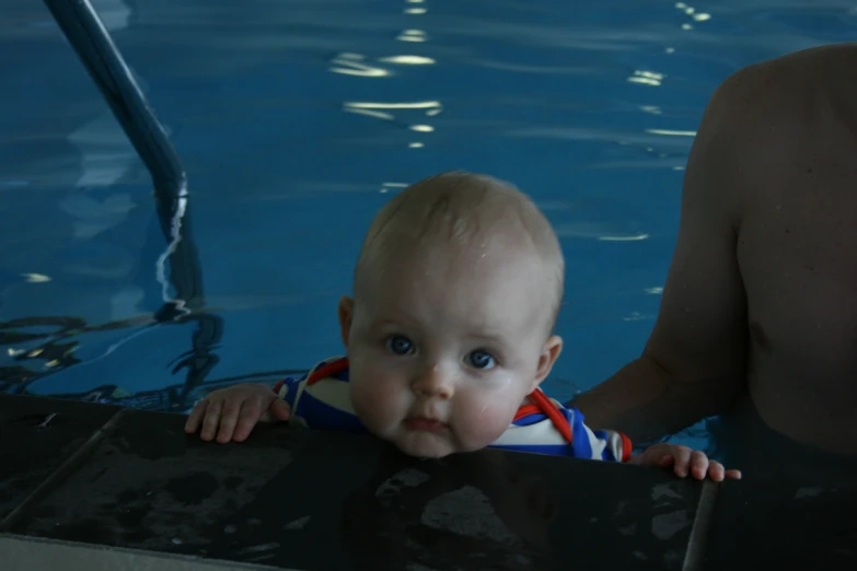 the baby is looking at the camera in the pool