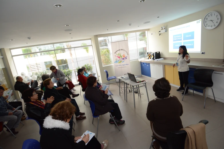 a group of people in chairs are listening to a woman on a projection screen