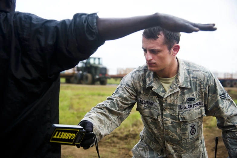 a military man adjusting another soldier's hand in front of a tractor